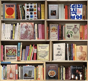 A diasec-mounted photograph by Max-Steven Grossman titled Cooking (2019), showcasing a bookshelf filled with cookbooks, culinary guides, and gourmet literature. Part of the Bookscapes series, this contemporary artwork celebrates food culture, fine dining,